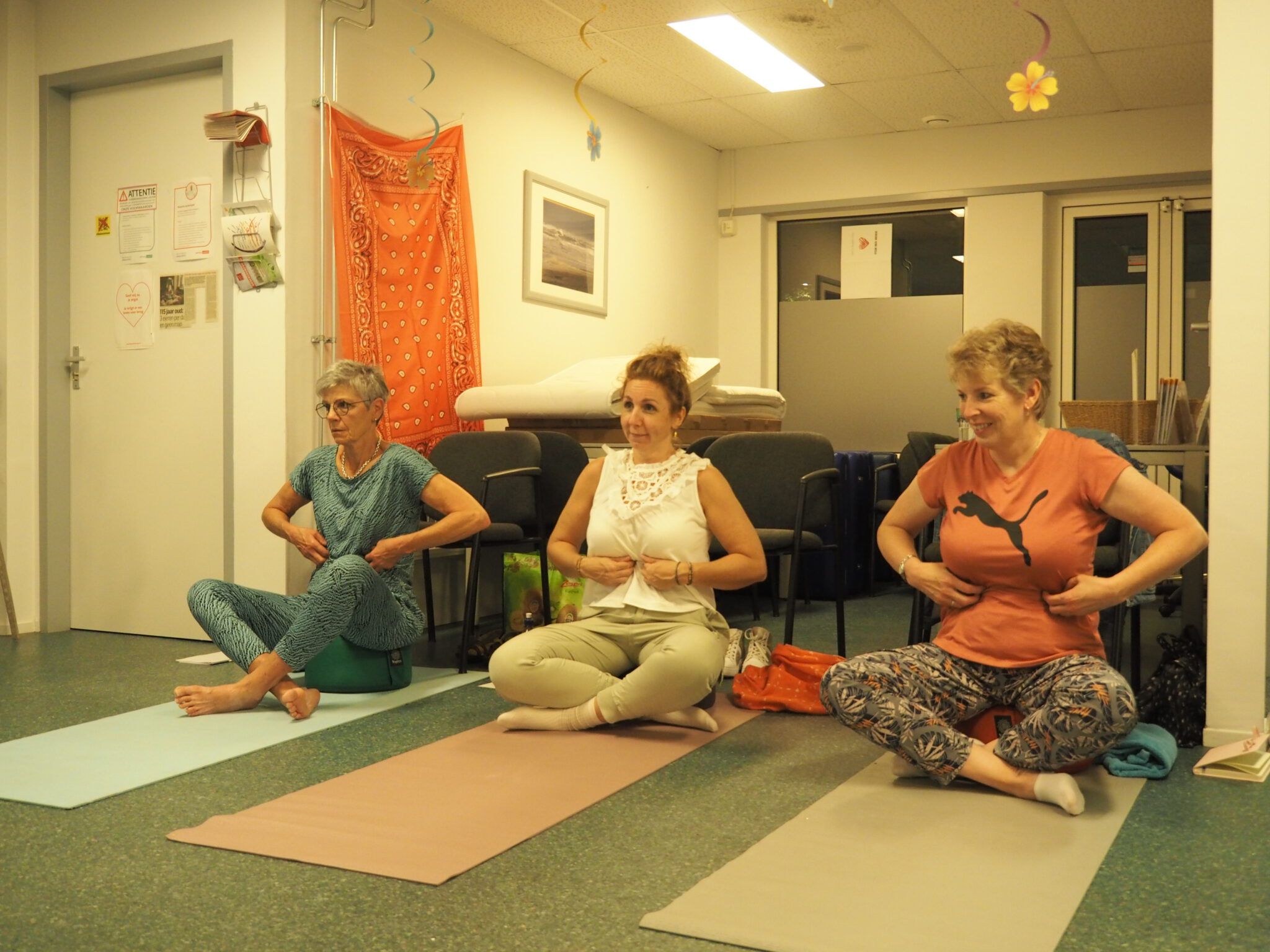 Drie deelnemers zitten op yogamatjes en voelen met hun handen op hun onderste ribben hoe ze ademen