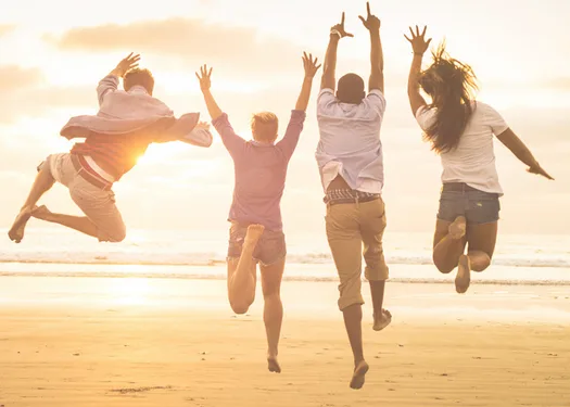 Vier mensen springen juichend in de lucht op het strand bij zonsondergang
