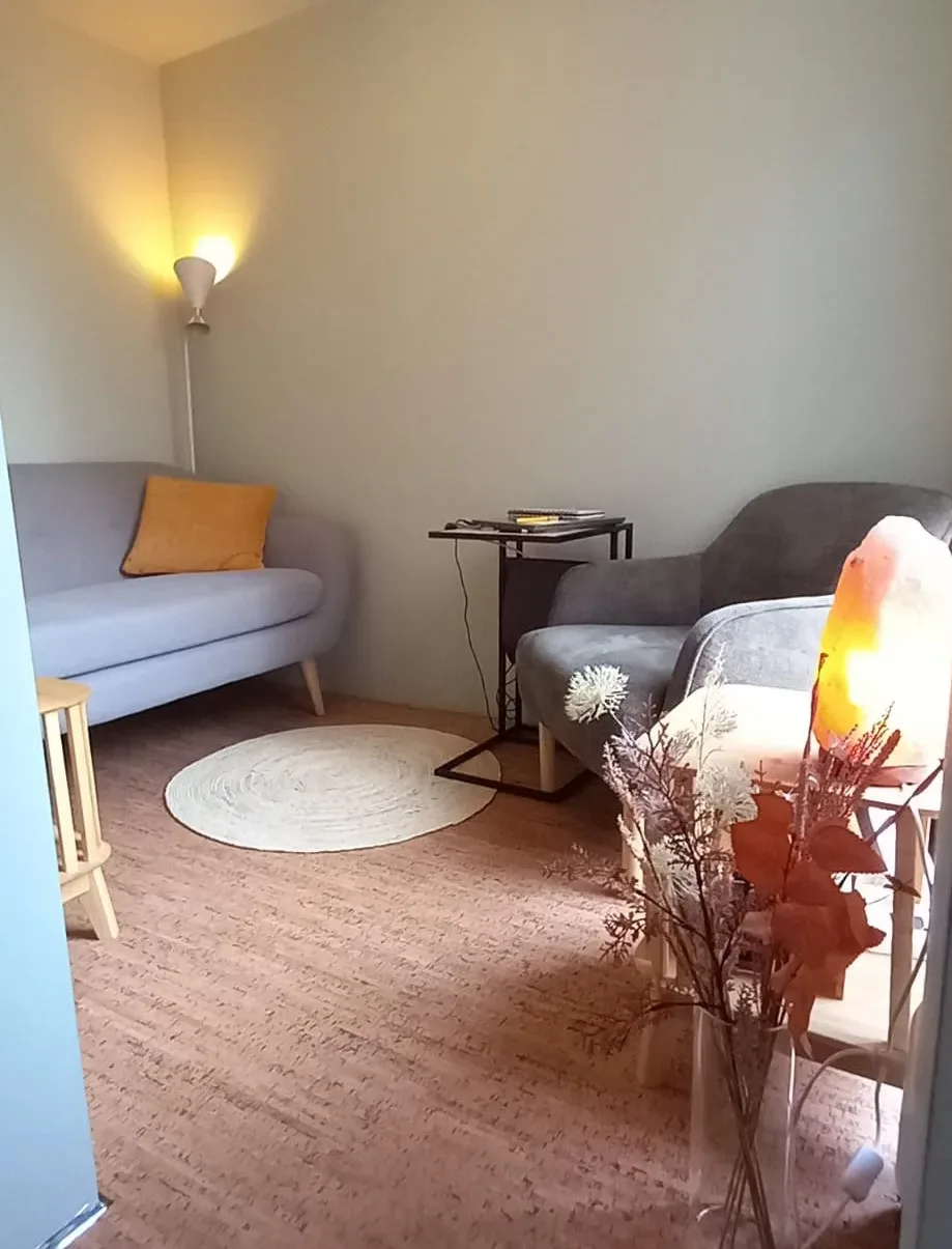 De praktijkruimte van Scan Your Health met een grijze bank, een fauteuil en een zoutlamp